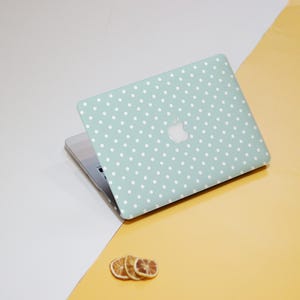 May include: A light green laptop with a white polka dot pattern. The Apple logo is visible on the lid. The laptop is open, revealing the keyboard. Three dried orange slices are in the foreground.