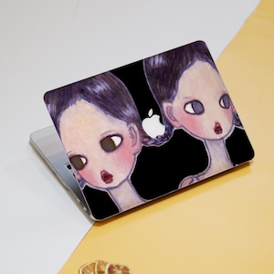 May include: Laptop cover featuring a watercolor illustration of two stylized female figures with dark hair, large eyes, and red lips. The background is black, and the Apple logo is visible. The cover is on a silver laptop.