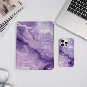 May include: A purple marble-effect notebook and phone case set. The notebook is rectangular, and the phone case has a camera cut-out. The design features swirling shades of purple and white. A laptop and a book are in the background.