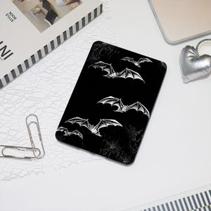 May include: Black and white illustration of bats flying against a black background with a spiderweb pattern.