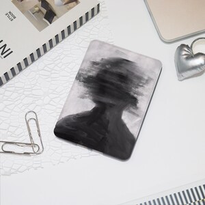 May include: A rectangular, abstract art mousepad featuring a grayscale image of a person's silhouette with a blurred face. The design is predominantly black and white, with brushstroke-like details. The mousepad is on a white surface, next to a silver heart-shaped object.