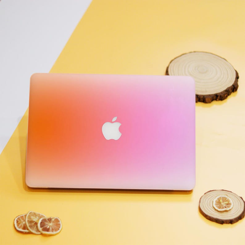 Puede incluir: Un ordenador port&aacute;til cerrado con un color degradado de rosa a naranja en la tapa. El logotipo de Apple es visible en la tapa.