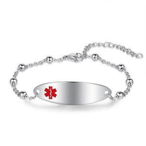 May include: A silver-toned medical alert bracelet with a polished finish. The oval-shaped plate features a red medical symbol. The bracelet has a chain with small, round beads and an adjustable clasp.