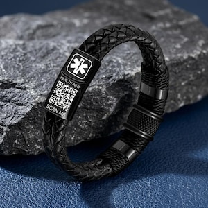 Peut inclure: Un bracelet d'alerte médicale en cuir tressé noir avec un fermoir métallique rectangulaire. Le fermoir présente un symbole de l'Étoile de Vie blanc, le texte HEALTH INFO, un code QR et le texte SCAN ME en blanc sur fond noir.