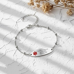 May include: A silver-colored medical alert bracelet with a chain and oval tag. The tag has the words "DIABETES INSULIN WARFARIN PENICILLINP" and a red medical symbol.