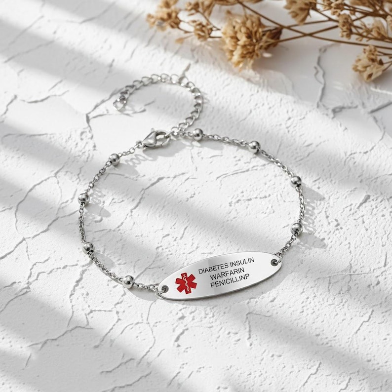 May include: A silver-colored medical alert bracelet with a chain and oval tag. The tag has the words "DIABETES INSULIN WARFARIN PENICILLINP" and a red medical symbol.