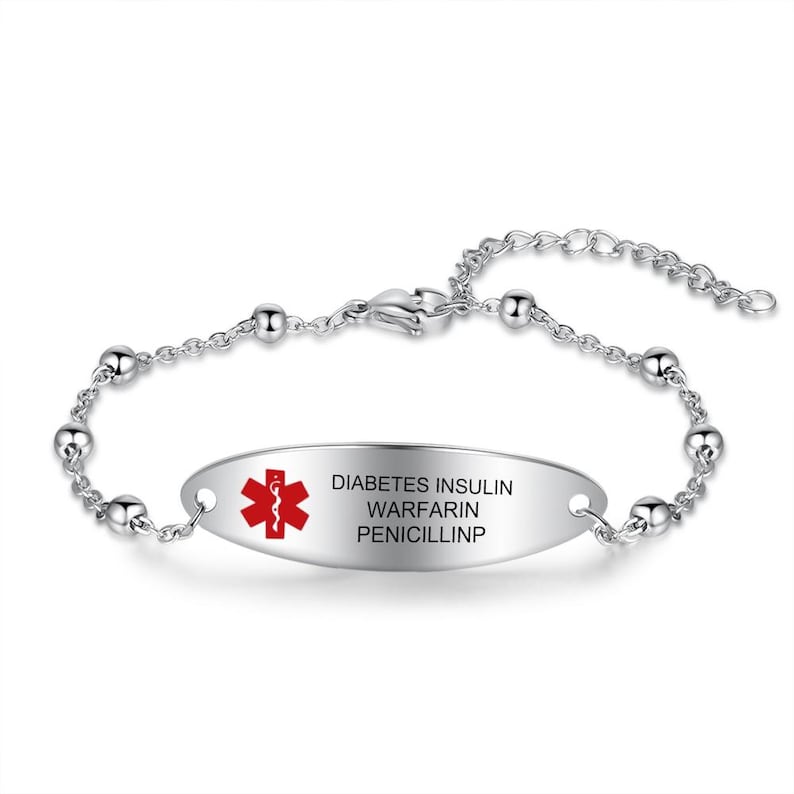 May include: A silver-toned medical alert bracelet. The oval-shaped plate has the red Star of Life symbol and the words "DIABETES INSULIN WARFARIN PENICILLINP" in black. The bracelet features a chain with small, round beads.