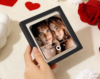 May include: A black framed photo with a picture of two people, with the text "Because You Live" and a music player interface. The background includes red hearts, white flowers, and a red rose.