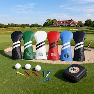 May include: A selection of golf club head covers in black, green, white, red, blue, and black. Each cover has a distinctive design with stripes and initials. Golf balls and tees are also present, alongside a black case.