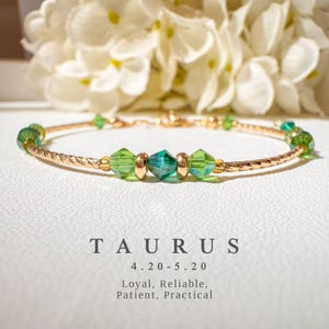 May include: Gold bracelet with green crystal beads. The bracelet features the zodiac sign Taurus and the dates 4.20-5.20. The text below reads "Loyal, Reliable, Patient, Practical."