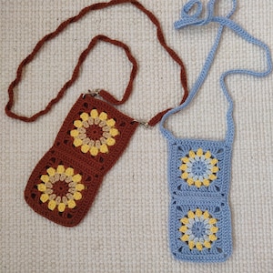 May include: Two crocheted bags with adjustable straps. The bag on the left is brown with yellow and tan flowers. The bag on the right is blue with yellow and white flowers.