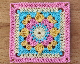 May include: A crocheted square with a multi-colored floral design in shades of pink, yellow, and blue.