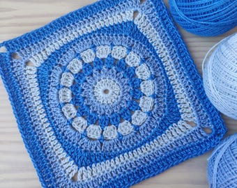 May include: A crocheted square with a circular design in shades of blue and white. The square is made with a variety of stitches, including single crochet, double crochet, and treble crochet. The center of the square features a circular design with a smaller circle in the center. The square is surrounded by a border of single crochet stitches.