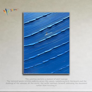 May include: A framed painting depicts a surfer on a blue wave. The textured waves stretch across the canvas. The painting's text reads: "This painting captures a moment of quiet courage."