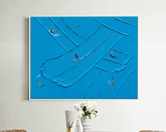 Op de afbeelding: Een rechthoekig wandkunstwerk met een levendige blauwe textuurachtergrond met dikke, zichtbare penseelstreken. Het kunstwerk toont verschillende kleine figuren van mensen die in het water zwemmen en surfen, wat een oceaanactiviteit suggereert.