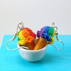 May include: Rainbow ice cream cone earrings with silver hooks. The ice cream is made of polymer clay and is a vibrant mix of red, orange, yellow, green, blue, and purple.