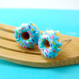 Könnte beinhalten: Ein Paar blaue Donut-Ohrringe mit bunten Streuseln. Die Ohrringe liegen auf einer Holzoberfläche.