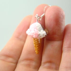 May include: A pair of silver earrings shaped like ice cream cones with pink, white, and brown ice cream. The ice cream is melting down the side of the cone.