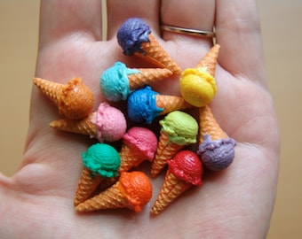 May include: A collection of miniature ice cream cones in various colors, including purple, blue, green, pink, orange, and yellow. The cones are arranged in a hand, with the tips of the cones pointing towards the viewer.
