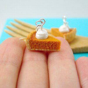 May include: A pair of miniature pumpkin pie earrings with a white dollop of whipped cream on top. The earrings are made of polymer clay and are attached to silver ear wires.