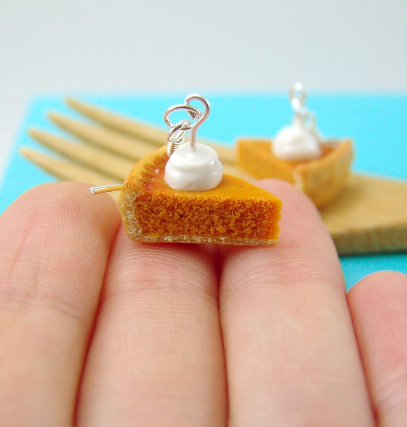 May include: A pair of miniature pumpkin pie earrings with a white dollop of whipped cream on top. The earrings are made of polymer clay and are attached to silver ear wires.