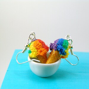 May include: A pair of rainbow and purple ice cream cone earrings. The earrings are made of polymer clay and are hanging from silver hooks.