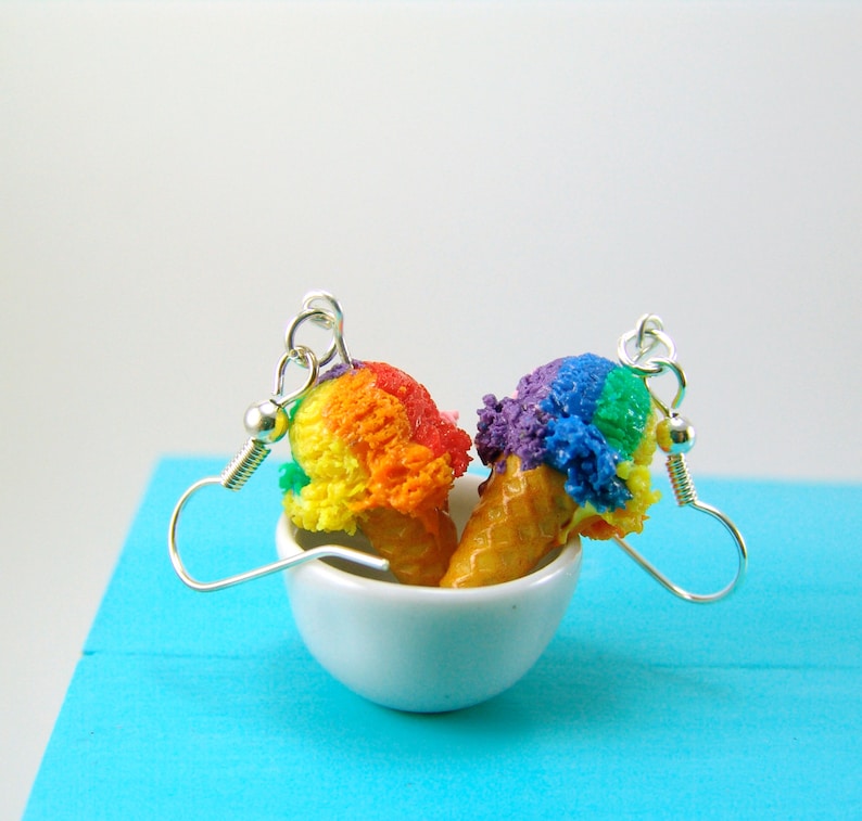 May include: A pair of rainbow and purple ice cream cone earrings. The earrings are made of polymer clay and are hanging from silver hooks.