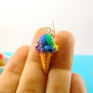May include: Rainbow ice cream cone earrings. The ice cream is purple, green, and yellow. The cone is a light brown color.