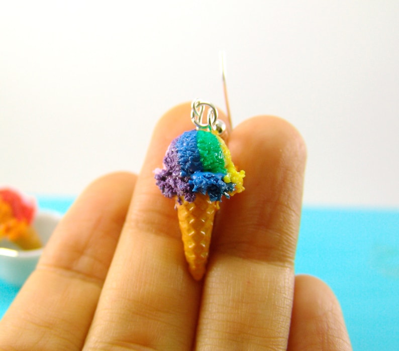 May include: Rainbow ice cream cone earrings. The ice cream is purple, green, and yellow. The cone is a light brown color.