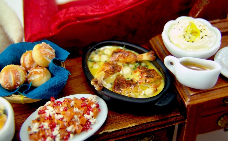 Puede incluir: Una mesa puesta con una variedad de platos, incluyendo una fuente para hornear con pollo y patatas, un bol de pur&eacute; de patatas, una salsera, un bol de ensalada de fruta y una cesta de panecillos.