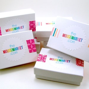 May include: Stack of white gift boxes with colorful washi tape and the text "the mousemarket.com" on each box.