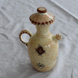 May include: A ceramic pitcher with a brown and white geometric design. The pitcher has a lid and a spout.