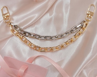 May include: A gold and silver chain with two clasps. The chain is on a pink satin background.