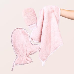 May include: A set of light pink plush bath accessories including a textured mitt and a soft towel. The items feature white trim with the repeating text HAVRELUXE printed in a dark color along the edges of the mitt and the towel border.