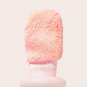 May include: A light peach-colored exfoliating mitt with a soft, fuzzy, textured surface. The mitt features a wide, elasticized wrist band in a matching light peach tone, with the brand name HAVRE LUXE printed in a subtle, light-colored font.