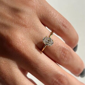 May include: A gold ring featuring a large, oval-cut diamond. The diamond is the focal point, set in a classic four-prong setting. The band is a thin, polished gold. The ring is shown on a person's finger.