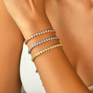 May include: Three tennis bracelets with round cubic zirconia stones. The bracelets are in gold, silver, and rose gold.