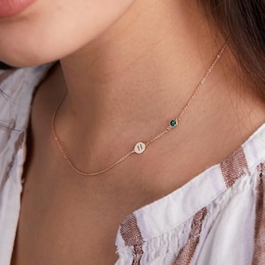 Può includere: Una collana con catena dorata con una piccola pietra verde e un ciondolo rotondo con la lettera "H" incisa.
