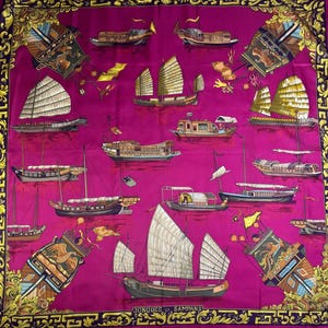 May include: A square silk scarf in vibrant magenta featuring a repeating pattern of various traditional Asian boats, including junks and sampans, with detailed sails and hulls. The border is decorated with a gold ornate scrollwork design.