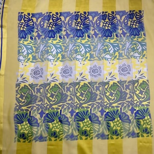 May include: A sheer yellow fabric with a repeating floral pattern in blue, green, and white. The design includes stylized flowers and leaves. Vertical yellow stripes border the floral pattern, with blue and white stripes along the edges.