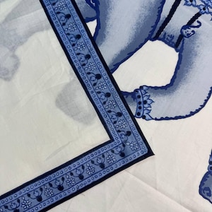 May include: White fabric with a blue elephant design. The border features a repeating floral pattern in blue. The elephant is depicted in a detailed, stylized manner, with intricate patterns and shading.
