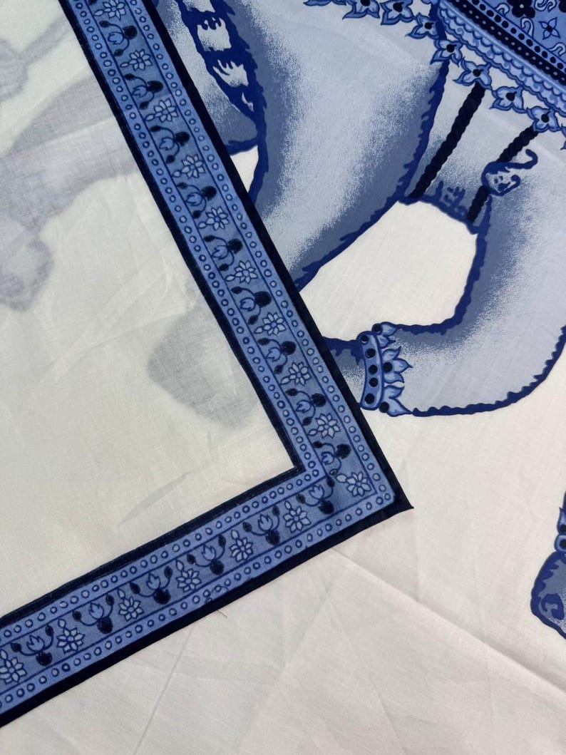 May include: White fabric with a blue elephant design. The border features a repeating floral pattern in blue. The elephant is depicted in a detailed, stylized manner, with intricate patterns and shading.