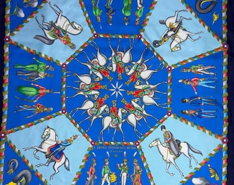 May include: Silk scarf with a detailed design of soldiers on horseback and in formation, set against a blue background. The scarf has a central starburst pattern and is bordered by a dark blue edge and a decorative rope-like trim. The text "L'ARMEE IMPERIALE RUSSE" is visible.