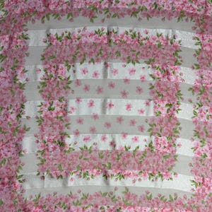 May include: A fabric with a floral pattern featuring pink cherry blossoms and green leaves. The design is arranged in horizontal stripes with a white background. The blossoms are clustered together, creating a delicate and feminine aesthetic.