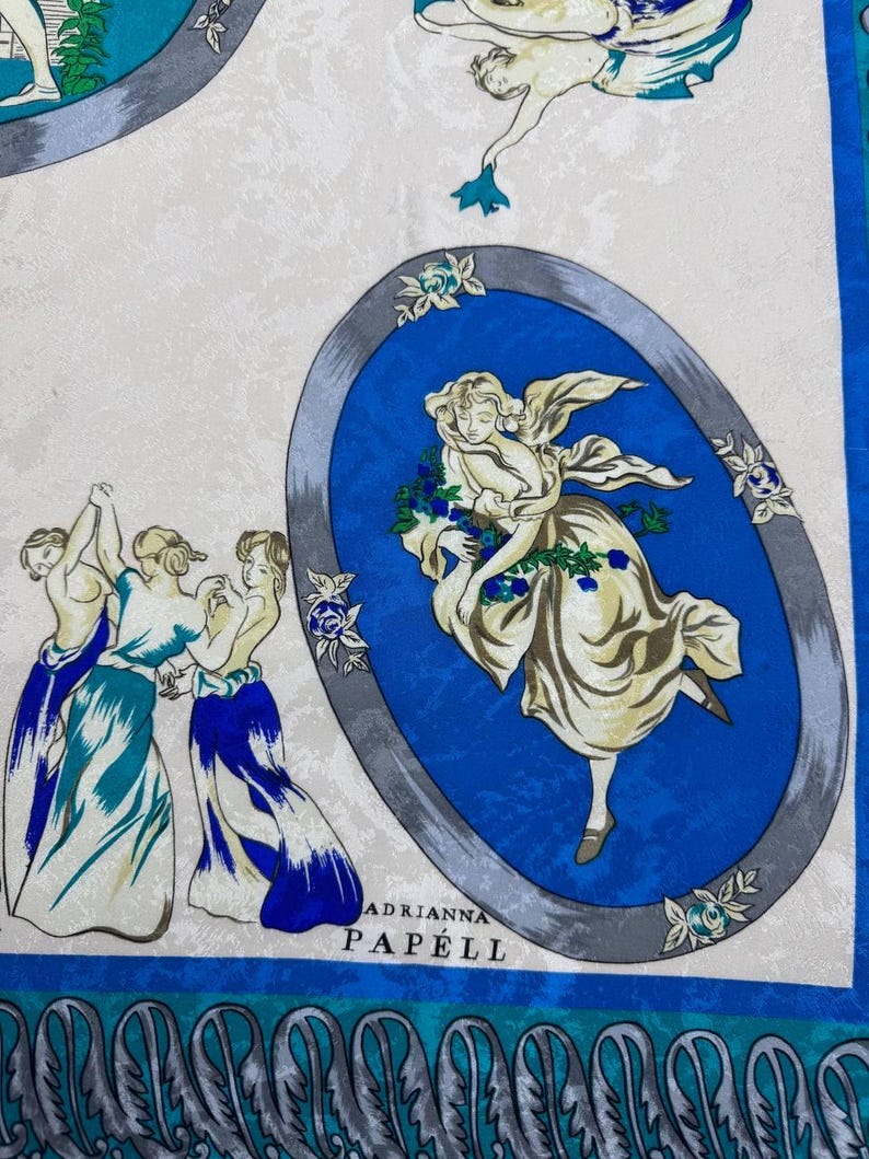 May include: A square silk scarf with a repeating pattern of classical figures in blue, white, and teal. The scarf features oval medallions with dancing figures and floral accents. The text "ADRIANNA PAP&Eacute;LL" is printed on the scarf.