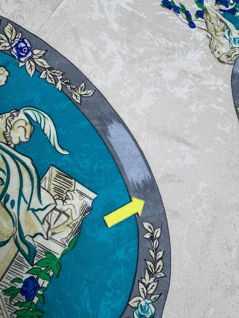 May include: A silk scarf with a teal and grey border, adorned with floral and classical figure illustrations. The scarf has a cream-coloured, textured background. Blue roses and green leaves accent the design.