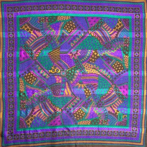 May include: Square silk scarf with a vibrant geometric pattern in shades of purple, green, gold, and brown. The scarf features a border with a repeating diamond design and a small logo in the corner.