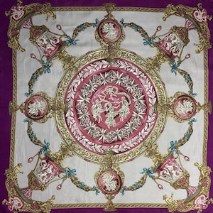 May include: Square silk scarf with a central pink medallion featuring dancing figures and starbursts, surrounded by gold filigree and decorative urns. The scarf has a white background with a deep purple border and accents of teal.
