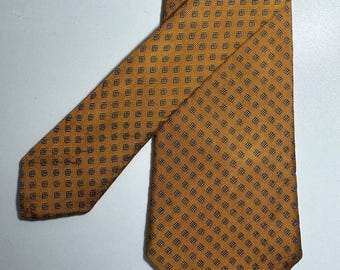 May include: Mustard-colored tie with a repeating pattern of small, dark blue squares. The tie is made of a smooth fabric and is neatly folded, showcasing its design. A classic accessory for formal or business attire.