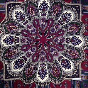 May include: A square scarf with a central floral paisley design in shades of burgundy, purple, green, and white. The scarf has a repeating border pattern and a small label in the lower right corner.
